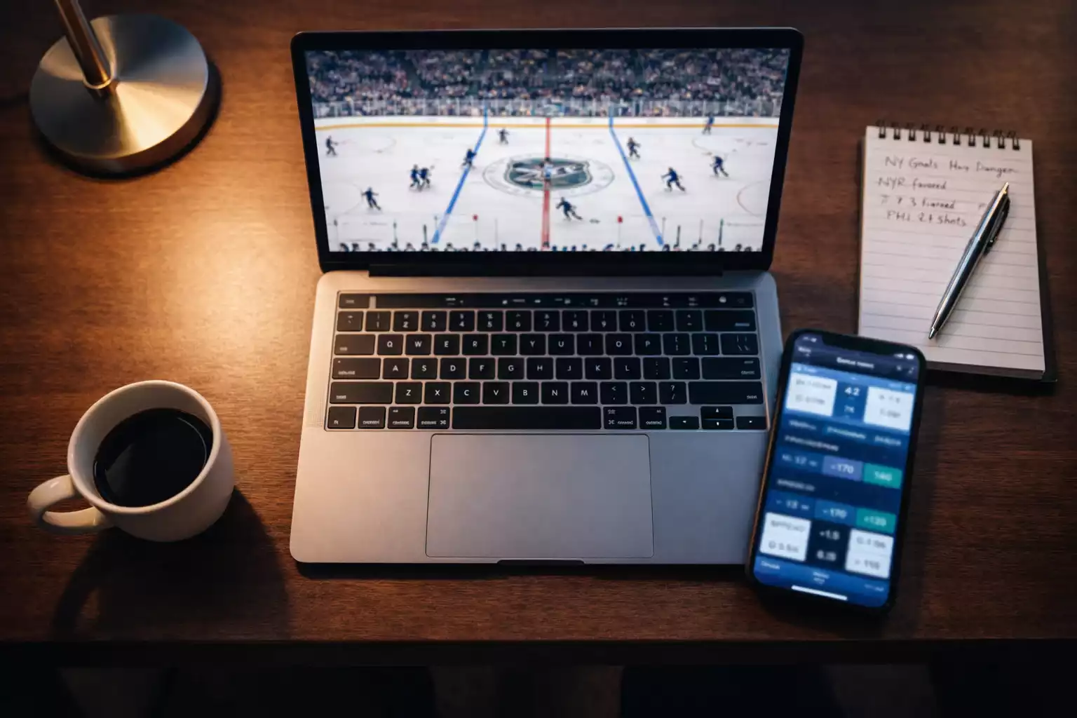Professional sports analyst workspace with laptop showing hockey game and smartphone displaying betting odds